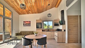A modern kitchen with wooden cabinets, a dining area with a round table and chairs, and a large window providing natural light.
