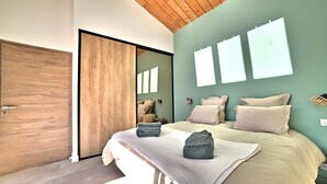 A modern bedroom with a wooden ceiling, a large mirror, a bed with beige bedding, and a wall-mounted light fixture.