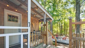 A wooden deck with a covered seating area, a door, and a view of a forested area.