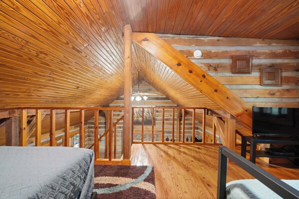 A log cabin interior with a wooden staircase, a bed, and a television.
