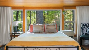 A bedroom with a large bed, two windows, a nightstand, and a chair.