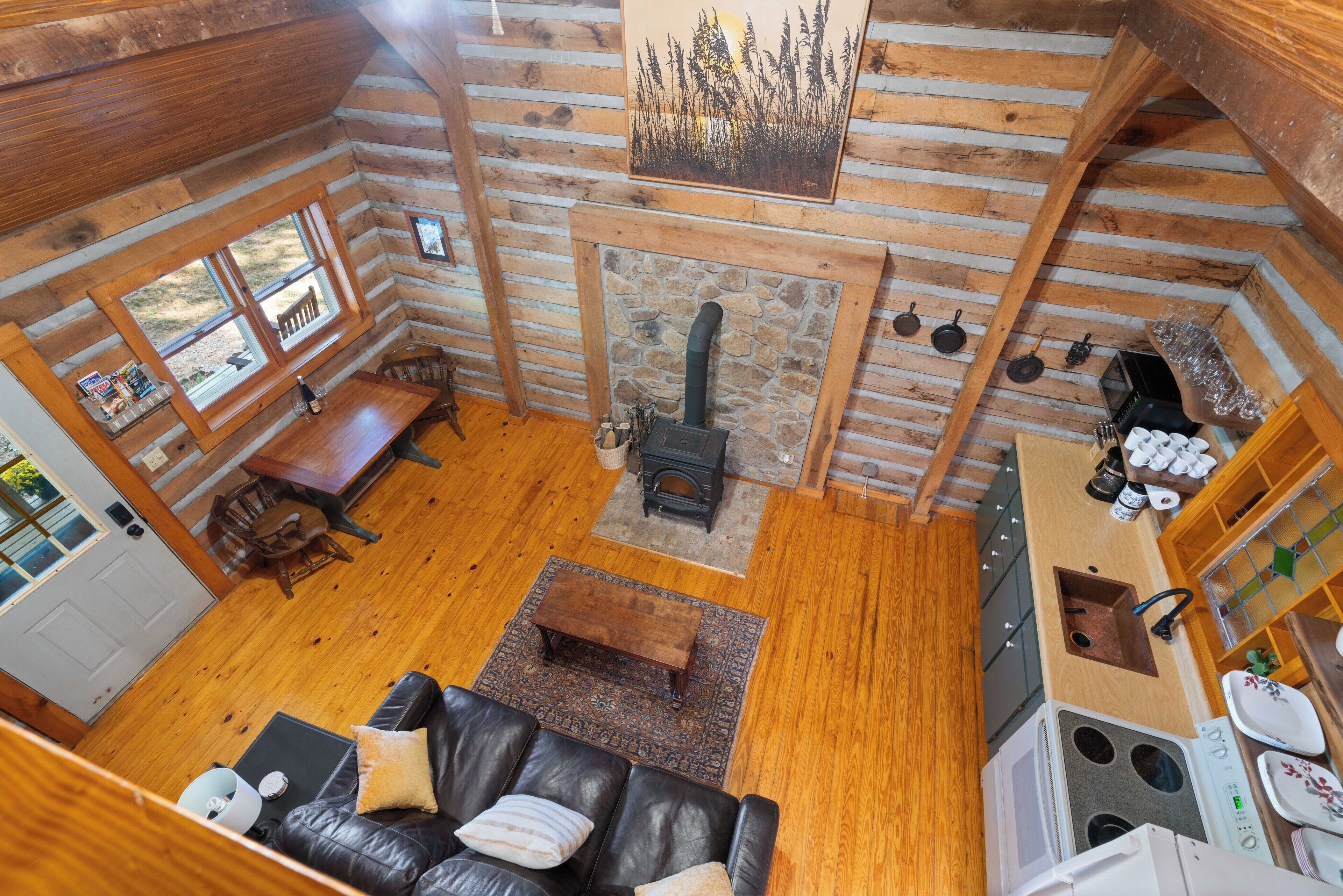 A cabin interior with a fireplace, wooden floors, a dining area, and a kitchen.
