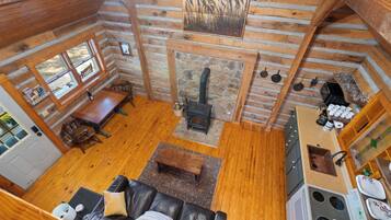 A cabin interior with a fireplace, wooden floors, a dining area, and a kitchen.