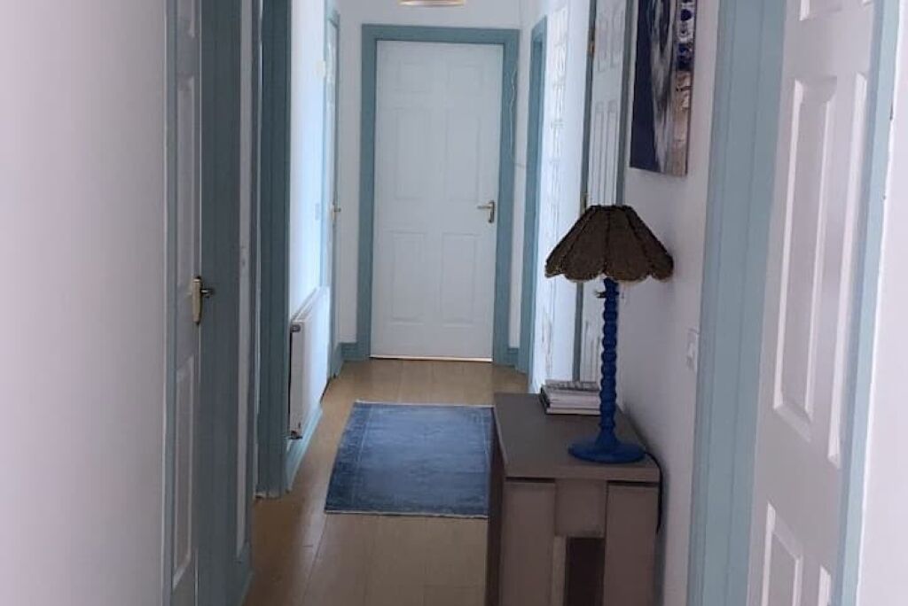 A hallway with a door at the end, a blue rug, and a lamp on a small table.