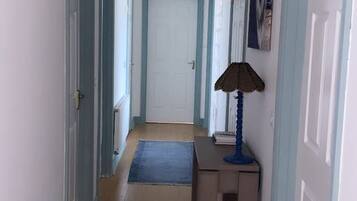 A hallway with a door at the end, a blue rug, and a lamp on a small table.