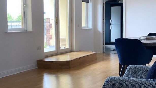 Un appartement moderne avec un plancher en bois, une chaise bleue et un escalier menant à un balcon.