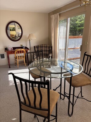 Une pièce comprenant une table ronde en verre entourée de quatre chaises, un bureau en bois avec une chaise, une lampe et un miroir accroché au mur.