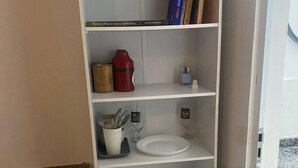 Un meuble blanc avec plusieurs étagères, un récipient rouge, une tasse blanche avec des couverts, un verre à vin et une assiette blanche.