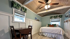 A bedroom with a bed, a desk, and chairs. There is a ceiling fan and a window with a view of trees. - Charming bungalow studio between the beach and downtown in welcoming St. Pete (St. Petersburg)