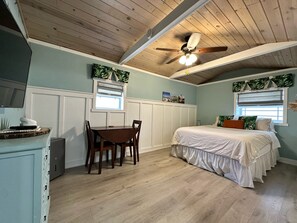 Una habitación con techo de madera, una cama con ropa blanca, una mesa de comedor con sillas y una ventana con vistas al exterior.