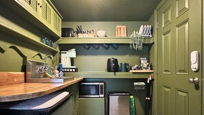 A compact kitchen with green cabinets, a microwave, a coffee maker, and a trash bin. - Charming bungalow studio between the beach and downtown in welcoming St. Pete (St. Petersburg)