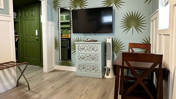 A living room with a wooden ceiling, a green door, a flat-screen TV, a decorative wall, and a dining area with a table and chairs. - Charming bungalow studio between the beach and downtown in welcoming St. Pete (St. Petersburg)