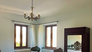 A bedroom with a bed, two chairs, a radiator, a window, and a mirror.