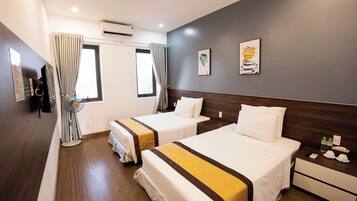 A hotel room with two beds, a wooden floor, a nightstand with a phone and toiletries, and a window with curtains.