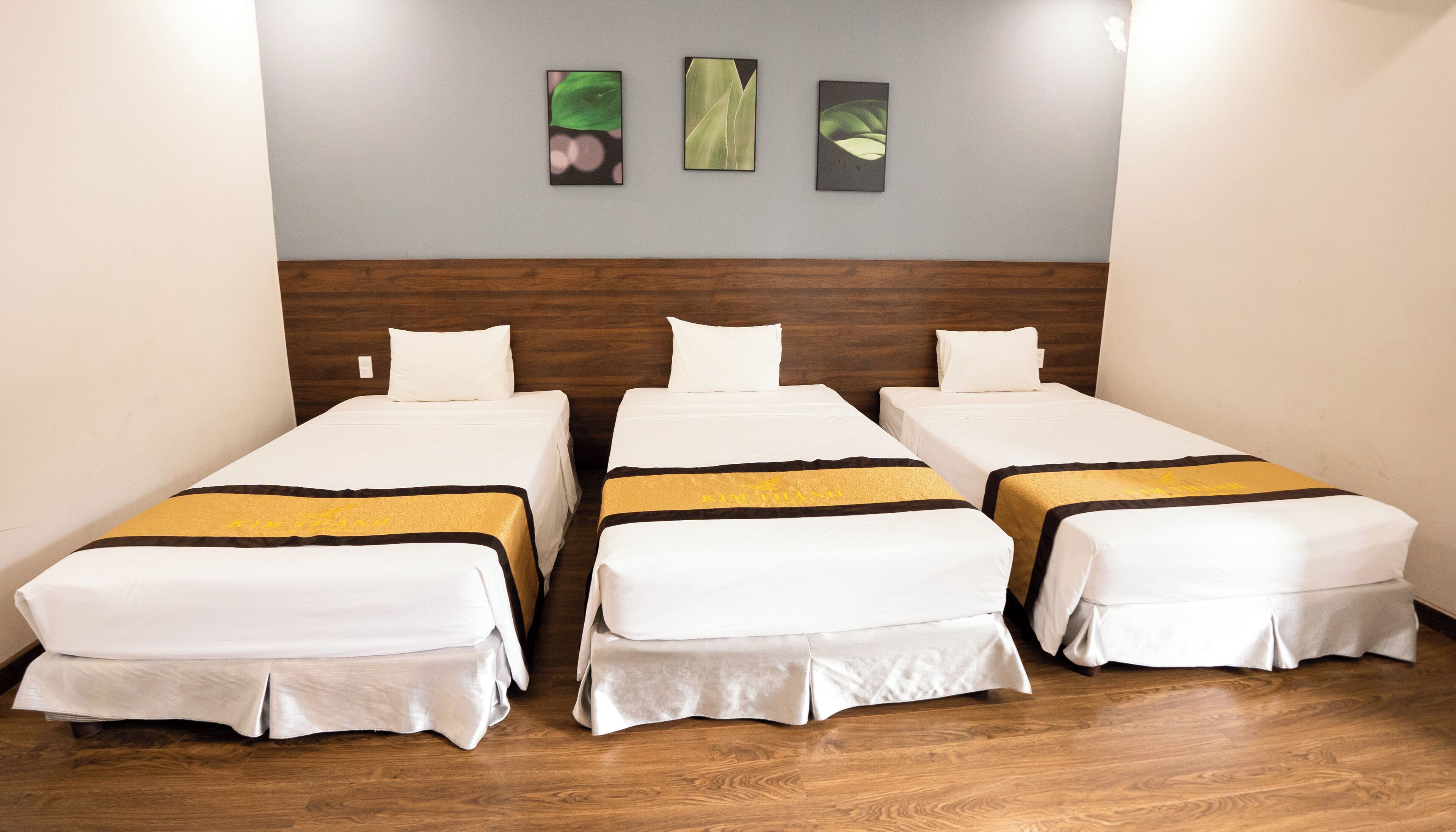 A hotel room with three single beds, wooden headboard, white bedding, and a wall with three framed artworks.