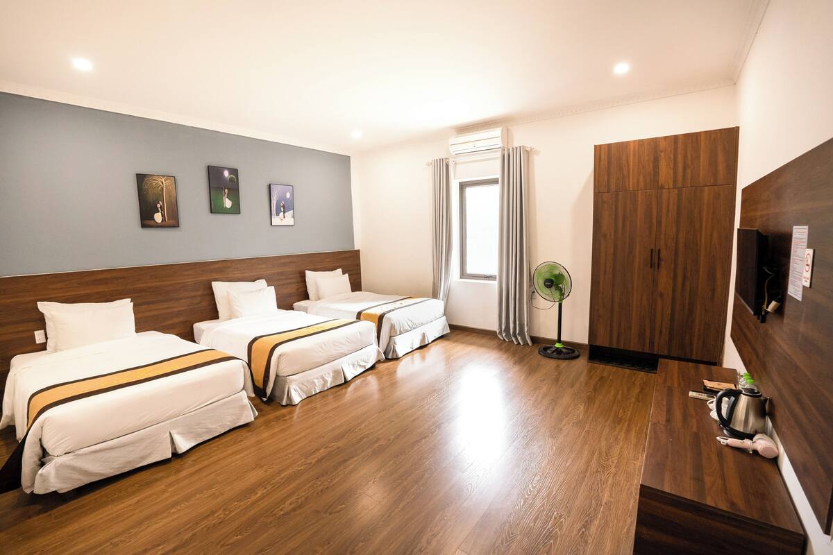 Habitación de hotel con dos camas, suelo de madera, televisor y ventana con cortinas.
