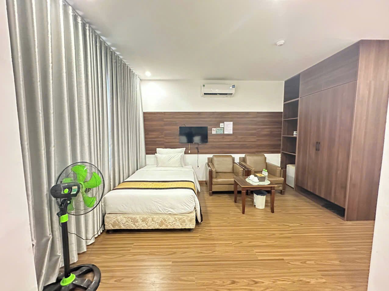 A hotel room with a bed, a desk, a chair, a TV, and a wardrobe.