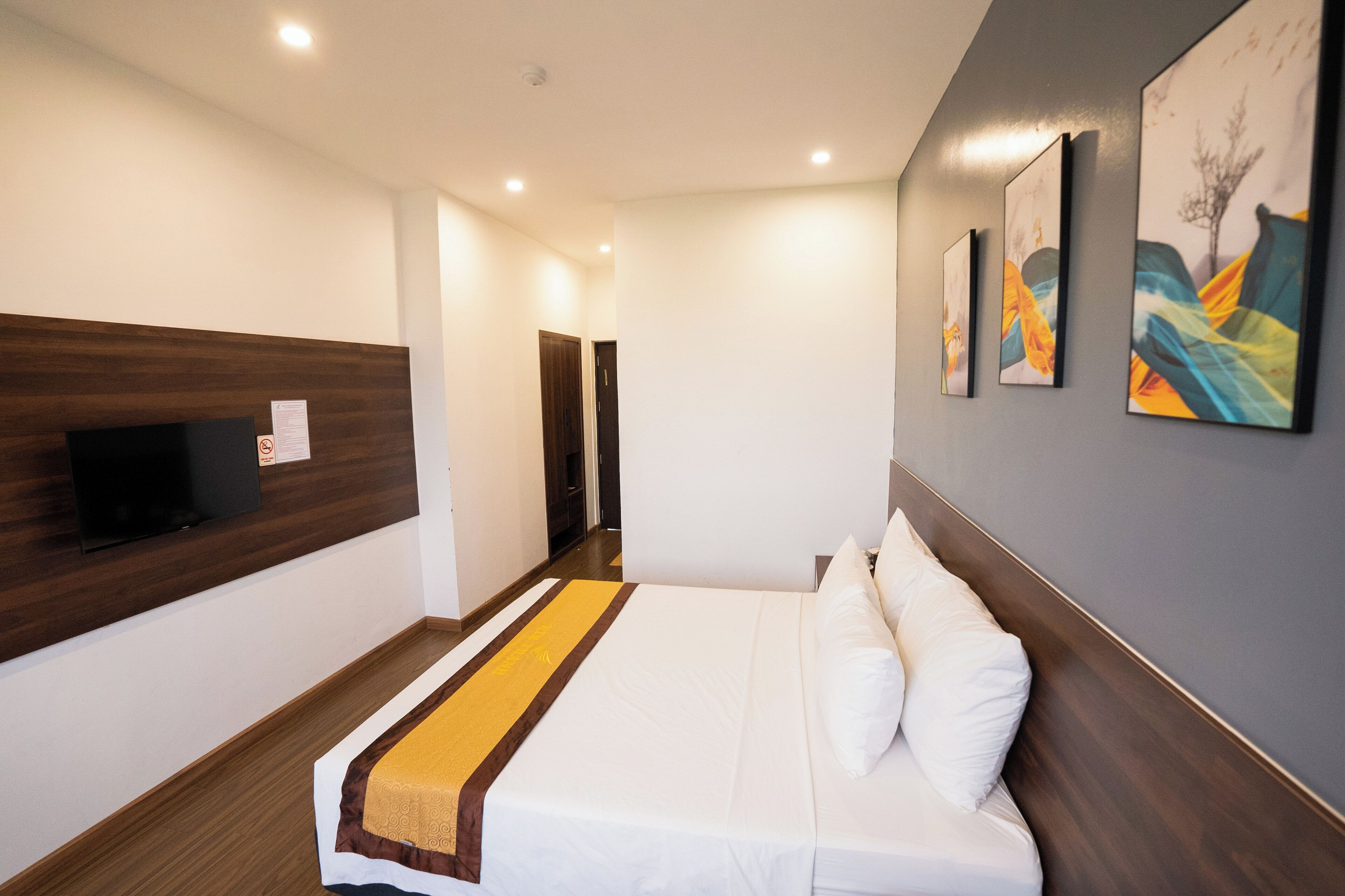 A hotel room with a bed, a flat-screen TV mounted on the wall, and artwork on the wall.