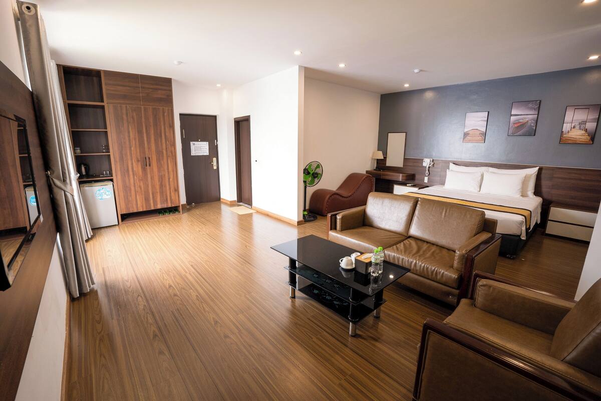 Una habitación de hotel moderna con suelo de madera, un sofá, una mesa de centro, una cama y un escritorio.