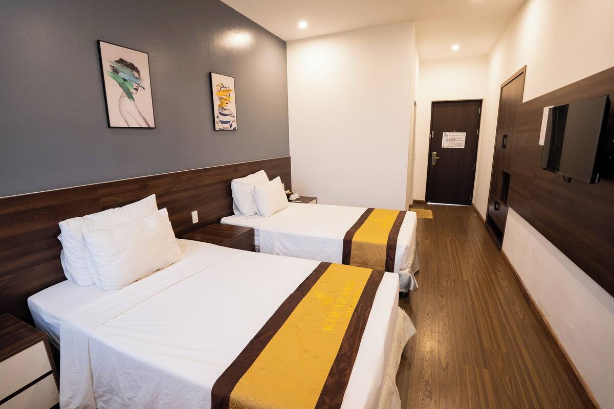 Una habitación de hotel con dos camas individuales, cabecera de madera, mesita de noche y televisor montado en la pared.