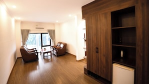 A modern living room with wooden flooring, a sofa, a chair, a small table, and a built-in wooden cabinet. - Kim Thanh Hotel (Vinh Phuc)