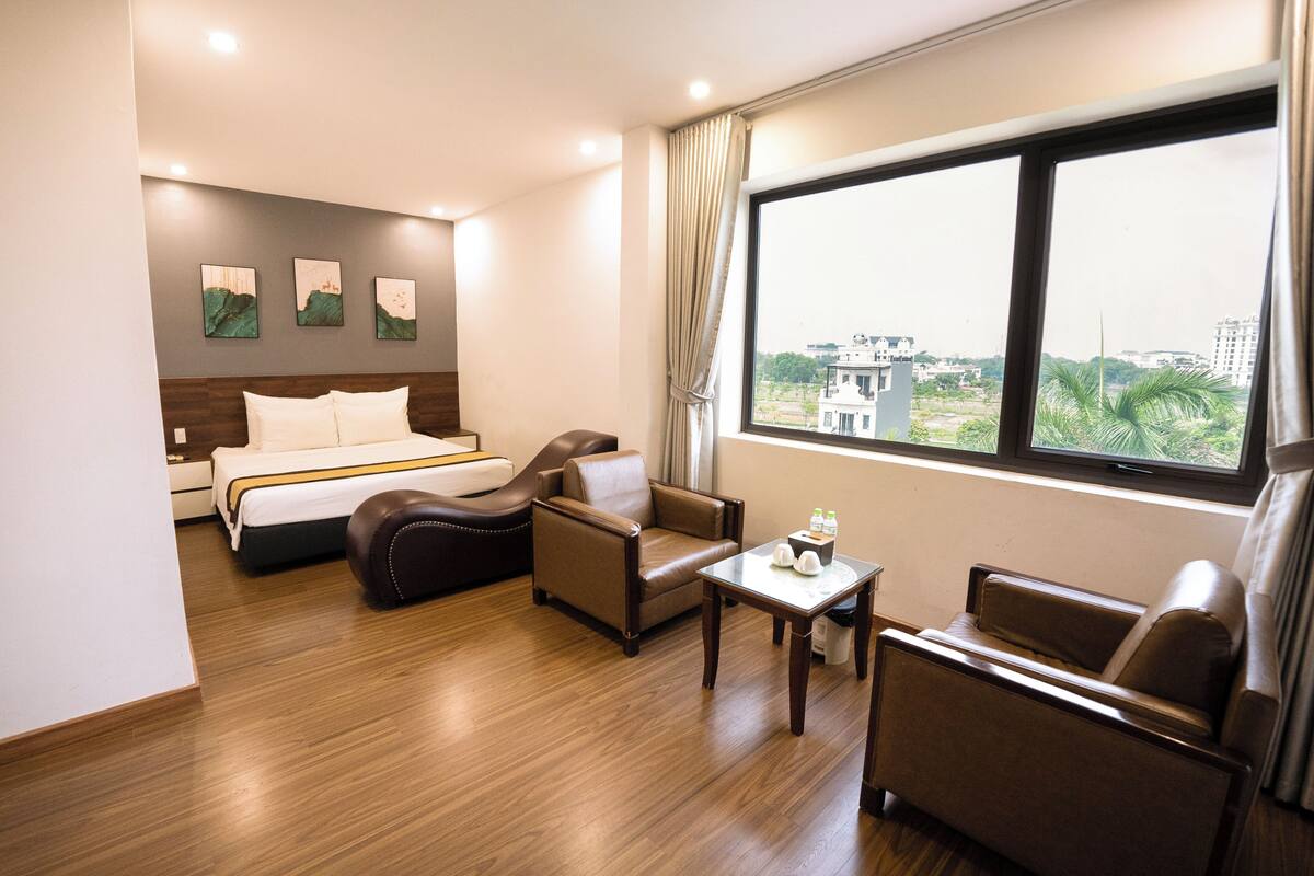 Habitación de hotel con una cama, dos sillones de cuero, una mesita pequeña y un ventanal con vistas a la ciudad.