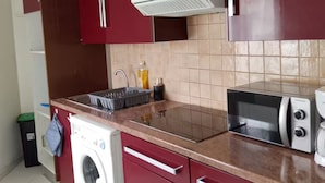 A kitchen with red cabinets, a washing machine, a microwave, and a sink. - Charming cottage in the heart of Saintes (Saintes)