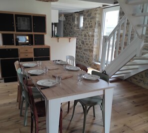 Un'area pranzo con un tavolo di legno apparecchiato per quattro persone, circondato da sedie. Sullo sfondo, si nota una scala che conduce a un piano superiore.