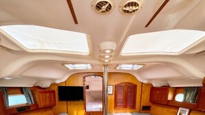 A compact interior with a sofa, a table, and a TV mounted on the wall. - Sailboat Stay • Marina Pools • Sleeps 4 • Stock Island, Key West (Key West)