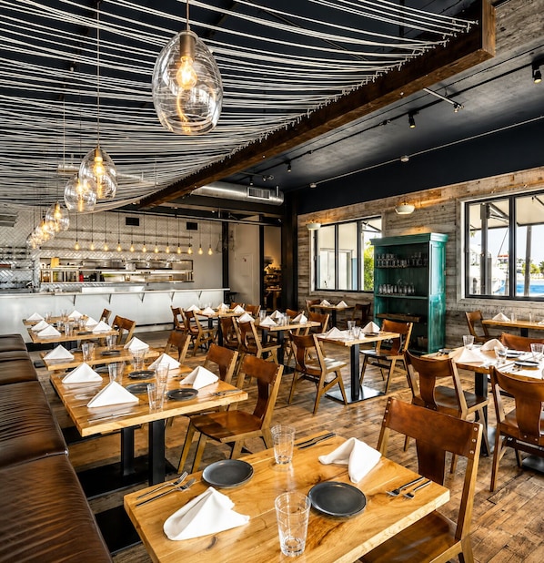 A restaurant with multiple tables, hanging pendant lights, and a view of the outdoors.