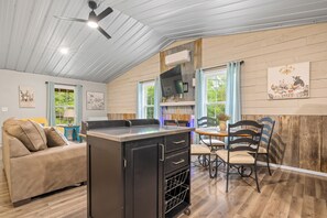 A cozy kitchen with a dining area, wooden walls, and a ceiling fan.