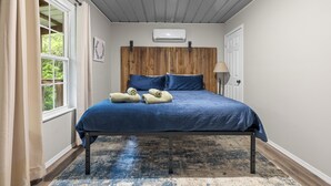 Ein Schlafzimmer mit einem Bett, einem Holzkopfende, einem Fenster und einer Wand-Klimaanlage.