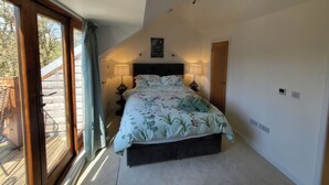 Un dormitorio con un ventanal grande, una cama con ropa de cama floral, dos lámparas de noche y una puerta.