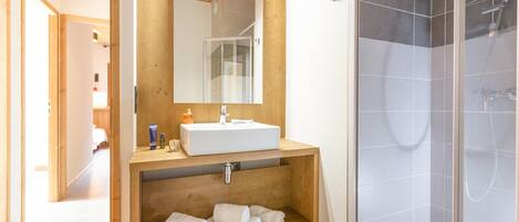A modern bathroom with a wooden vanity, a large mirror, a shower enclosure, and a walk-in shower.