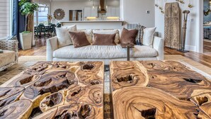 En rummelig stue med en stor sofa, et sofabord med et unikt trædesign, og et køkken i baggrunden.