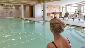 Una piscina interior con vista despejada al borde, una pared de madera con un letrero y un área de descanso con sillones y una persona relajándose.