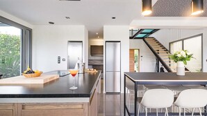 Una cocina moderna con una isla grande, electrodomésticos de acero inoxidable y un comedor con sillas blancas.