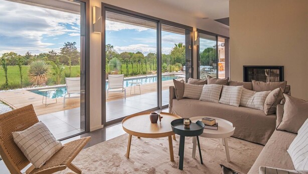 Una sala de estar moderna con un ventanal grande que da a una piscina y abundante vegetación.