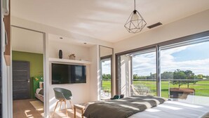 Un dormitorio moderno con una cama grande, un televisor montado en la pared y un balcón con vistas al campo.