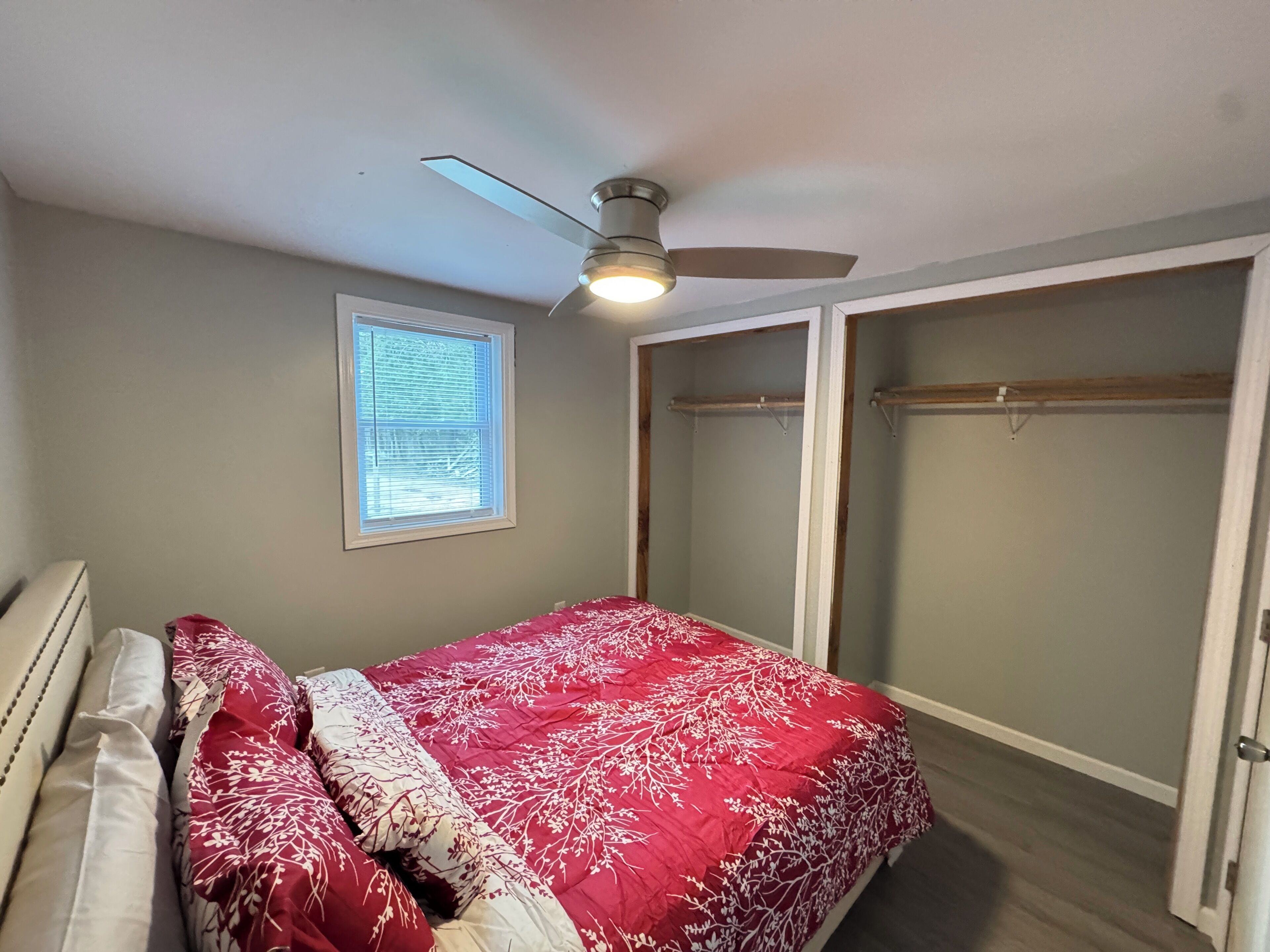 A bedroom with a bed, a ceiling fan, a window, and a walk-in closet.