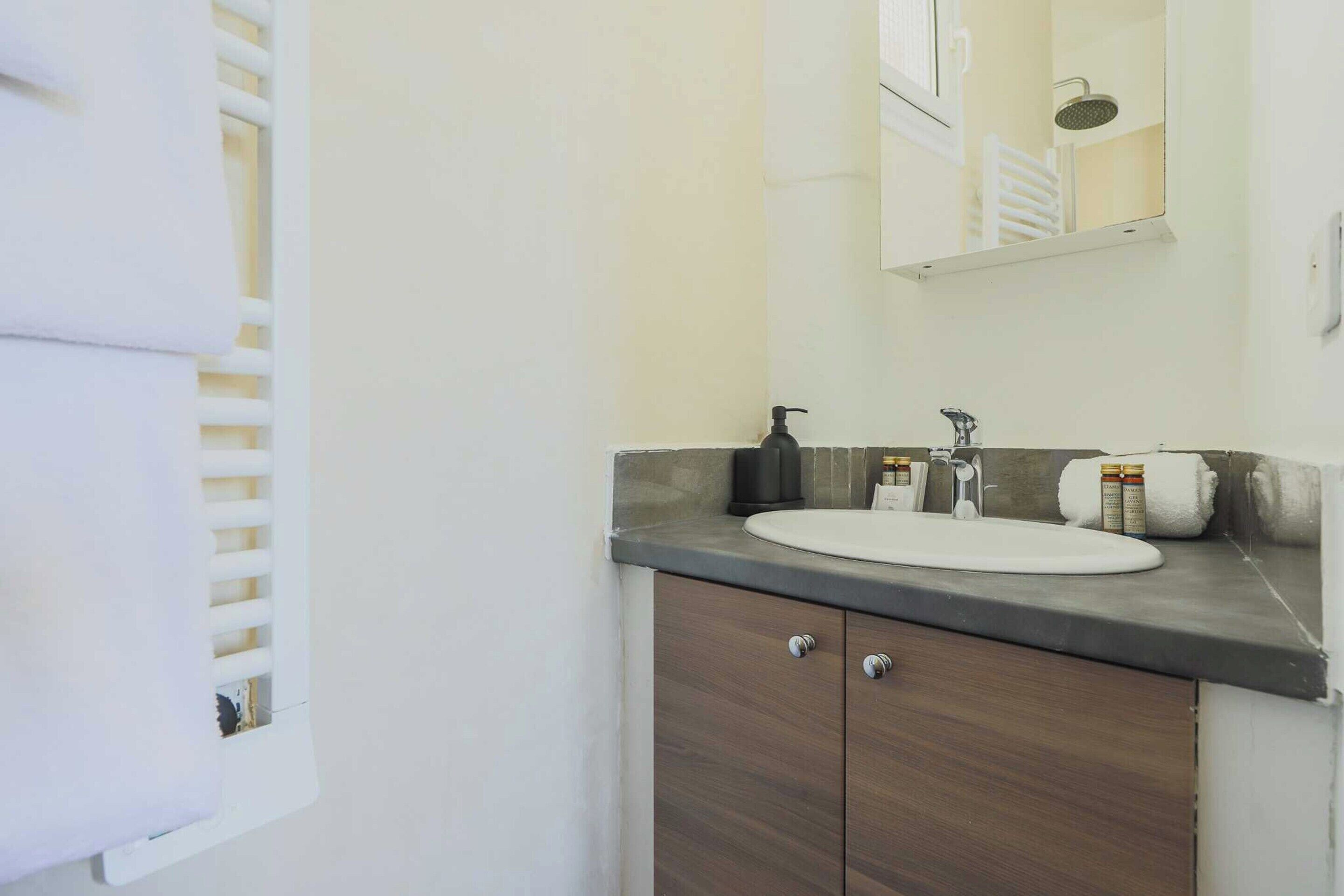 A bathroom with a white sink, a mirror, a shower, and a towel rack.
