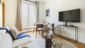 A modern living room with a sofa, a dining table set for four, a flat-screen TV, and a large window with curtains. - Charming Flat -1br-4p- Paris 17e (Paris)