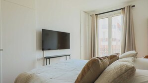 A bedroom with a bed, a TV mounted on the wall, and a window with curtains. - Charming Flat -1br-4p- Paris 17e (Paris)