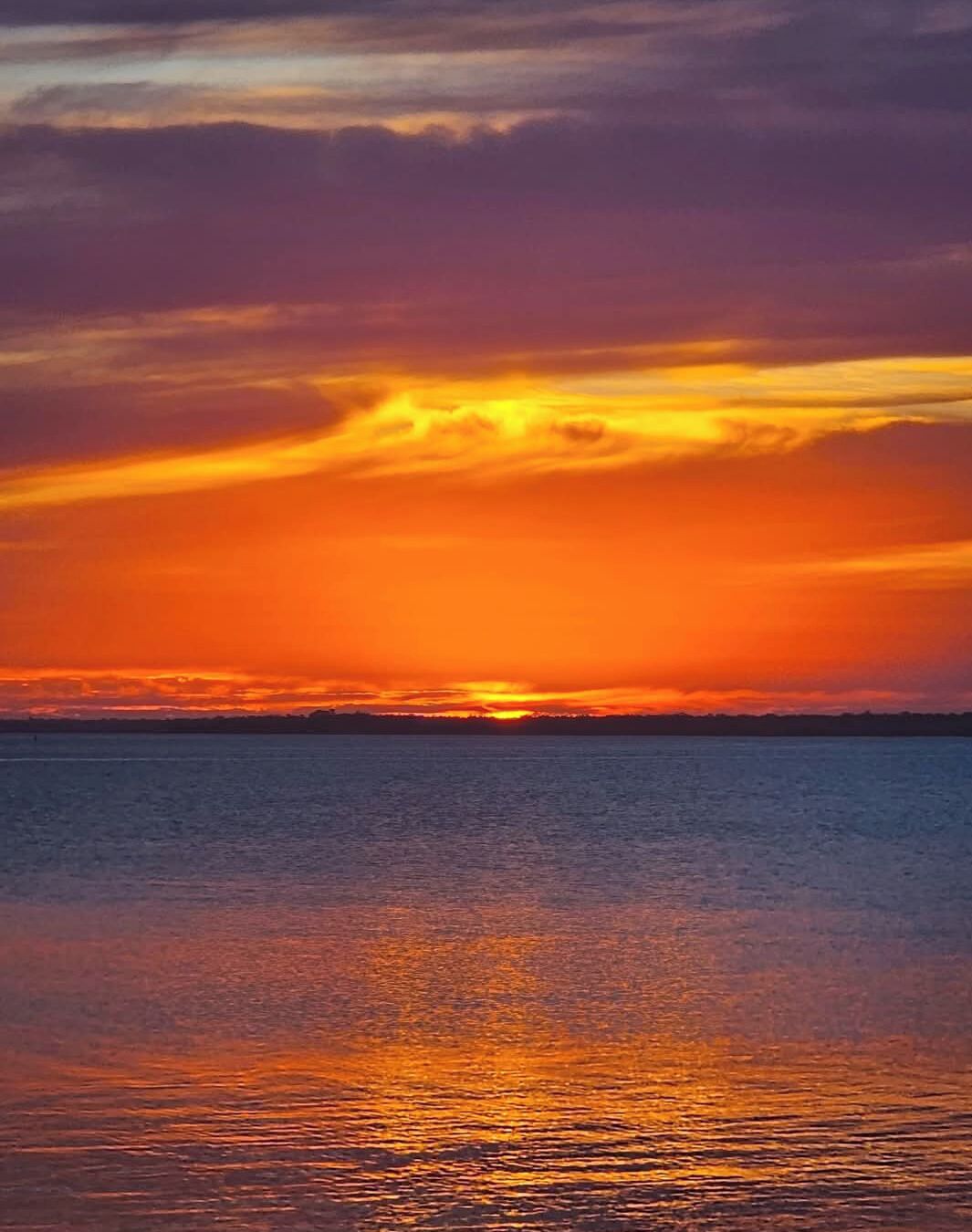 Un atardecer sobre un cuerpo de agua tranquilo, con un horizonte despejado.