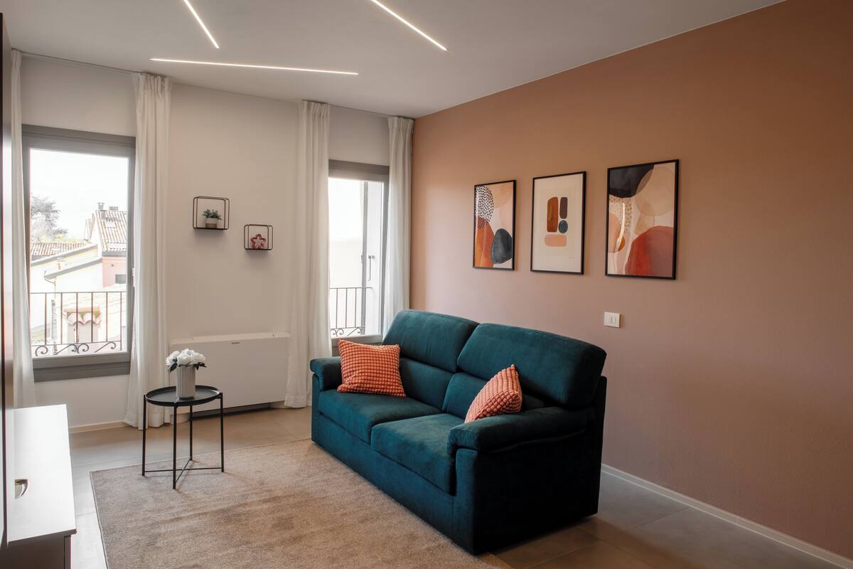 A modern living room with a teal sofa, a small side table, and a view of a balcony.