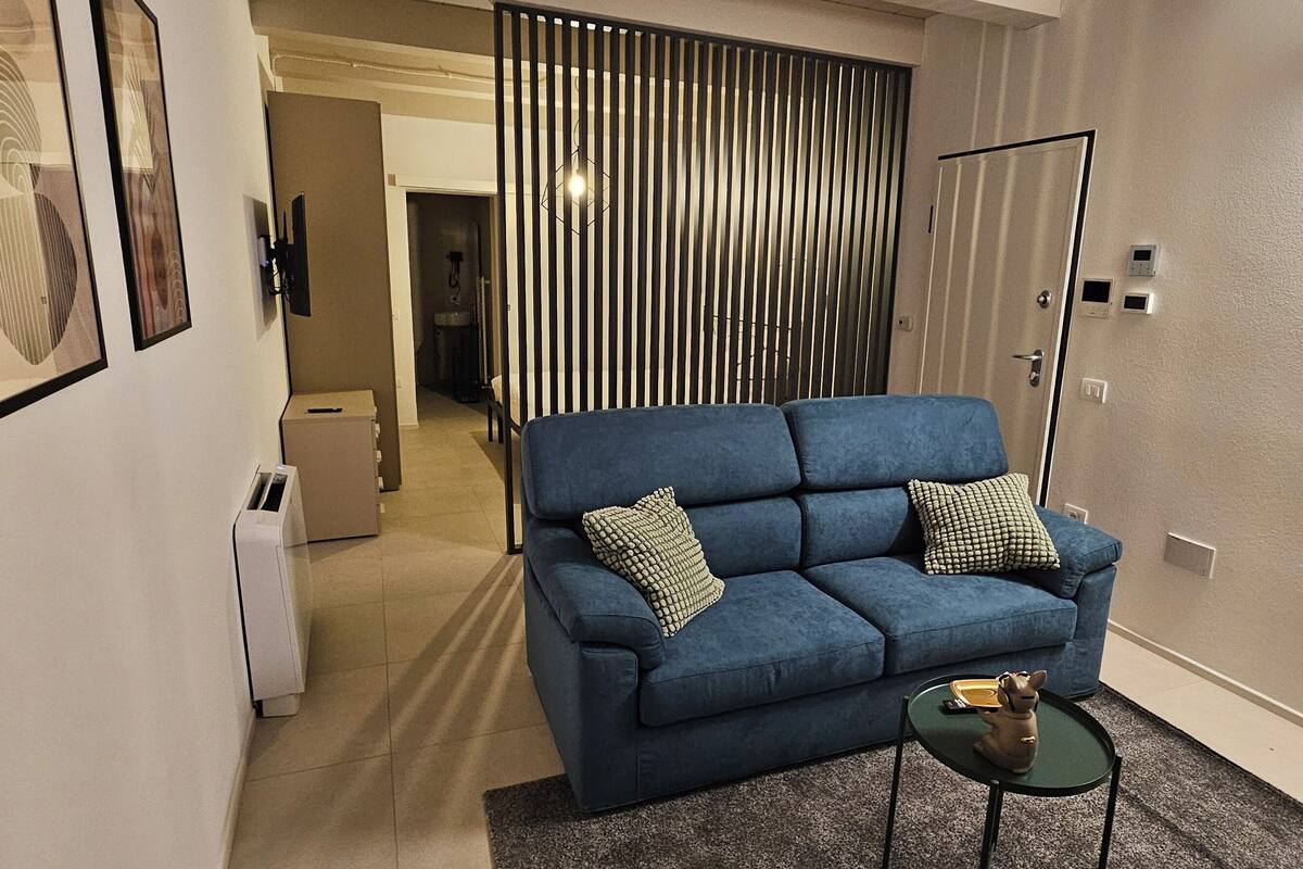 A modern living room with a blue sofa, two pillows, a small table with a figurine, and a sliding door in the background.