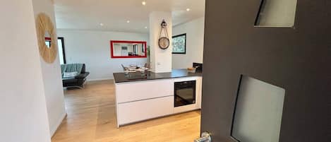 A modern kitchen with a central island, a dining area with a sofa, and a living room with a sofa and a TV.