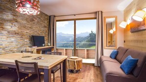 Ein gemütliches Zimmer mit Holztisch, Stühlen, einer Couch und einem großen Fenster mit Blick auf die Berge.
