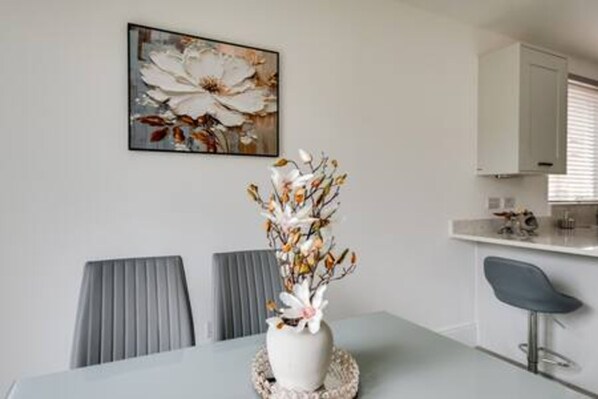 Un comedor con una mesa, sillas, un florero con flores y un cuadro en la pared.