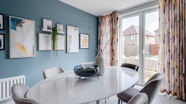 A dining area with a white table and chairs, framed artwork on the wall, and a view of the outside.